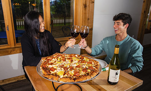 couple toasting wine before enjoying a large pizza