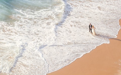 Aerial view of a bride and groom walking in the water at the beach at daytime
