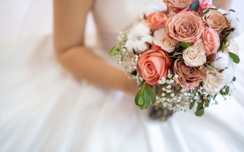 Closeup view of a body of a bride holding a  boutique roses in a pale accents