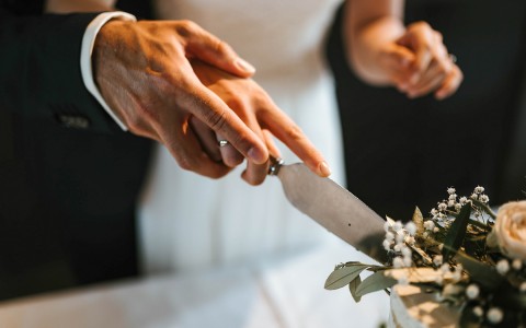 Closeup view of the hands of bride and groom cutting a cake