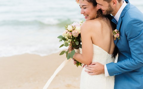 Bride and groom hugging and smiling at the beach at daytime