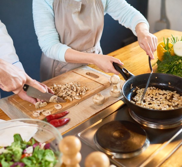 Male chef chopping mushrooms and a female chef cooking some food