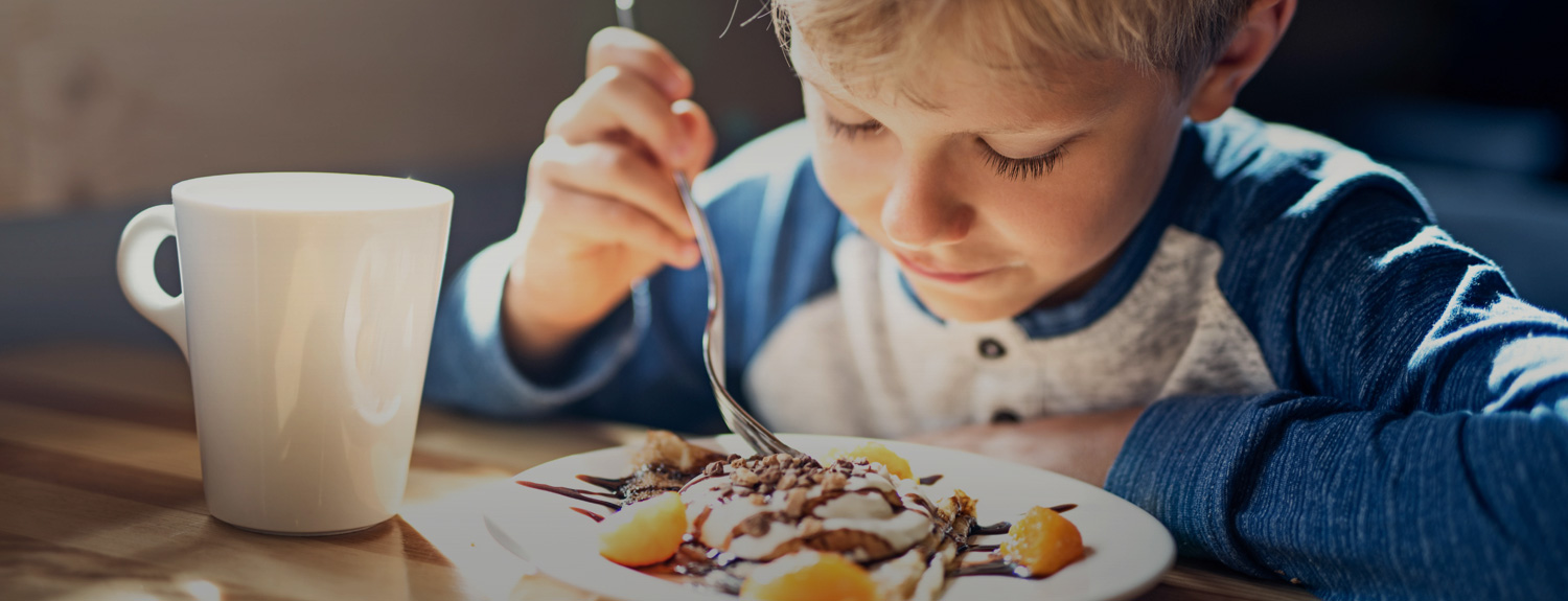 boy with a fork looking at his food and a cup of coffee next to the plate
