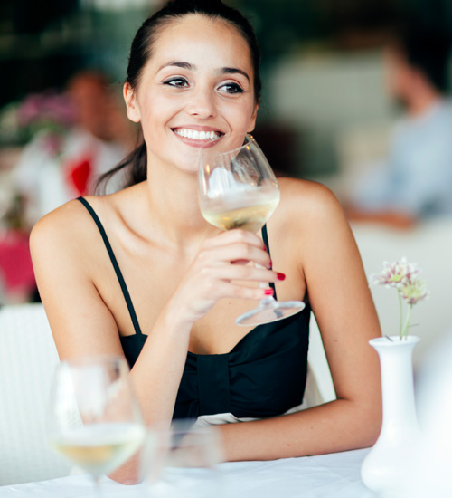 Lady smiling while she is holding a glass of white wine looking forward