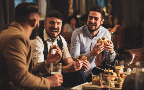 Group of friends laughing as they eat their burgers & drink bourbon