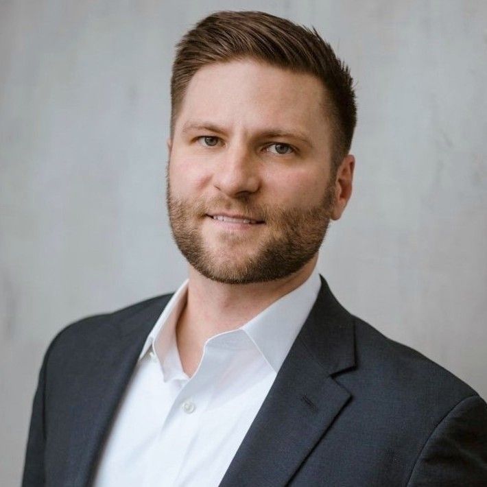 Headshot of a blond man with a beard in a suit