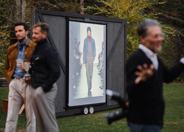 people at an event with a screen showing a fashion show