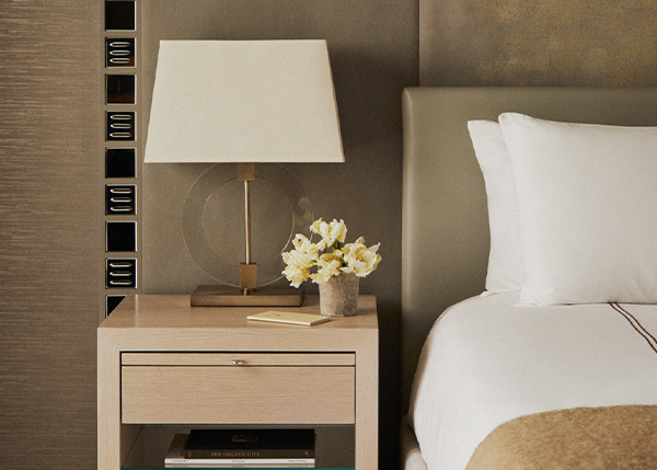 partial view of an elegant bed next to a wooden night stand with a lamp and flowers on top