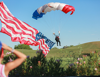 Parachuter landing while pulling an American flag trailing behind him