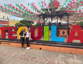 Two women standing in front of a sculpture of the word "tequila"