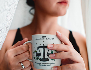 Woman holding a mug with the Libra scaled painted on it