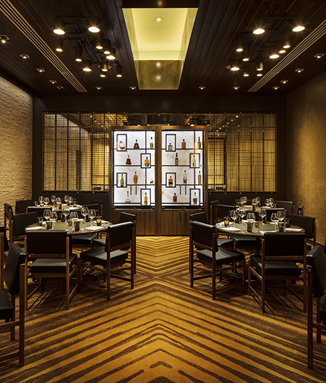 a dim lit dining room with a wall showcasing various bottle of liquor