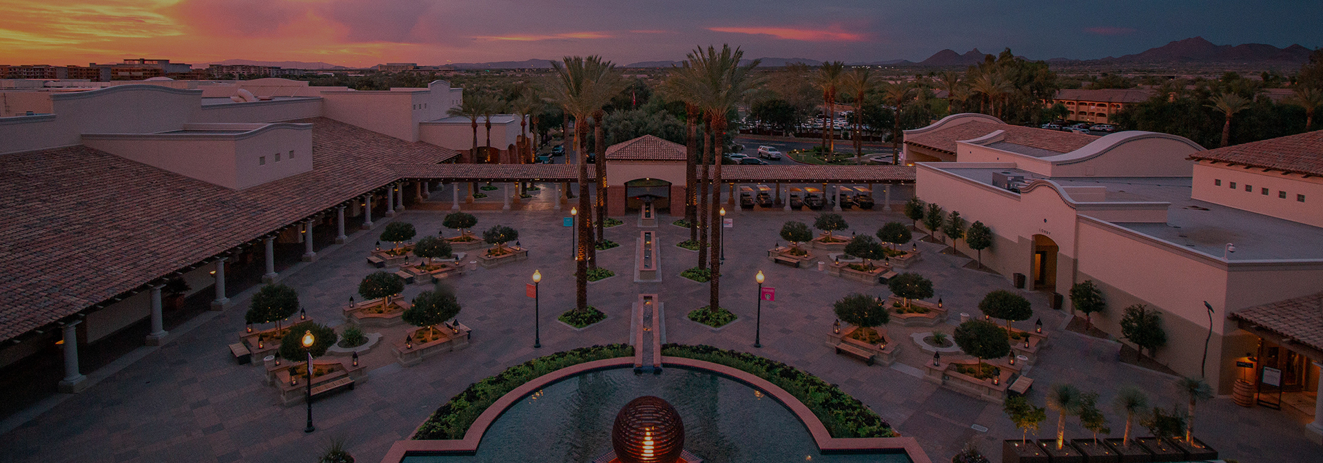 Drone shot of the resort fountain and gathering area with the sun setting in the distance