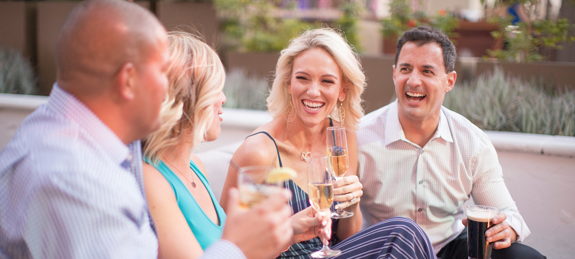 a group of friends smiling at each other while sitting outside with glasses in their hands