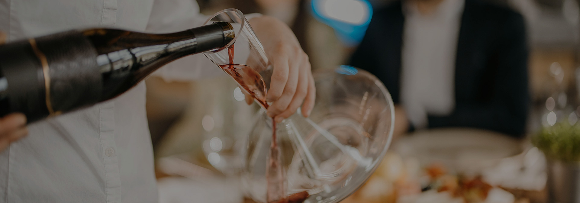 A person pouring a bottle of red wine into a glass decanter