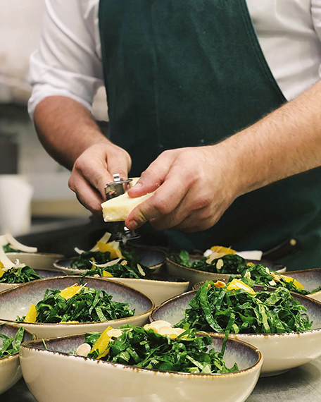 chef adding parmesan cheese to several salads