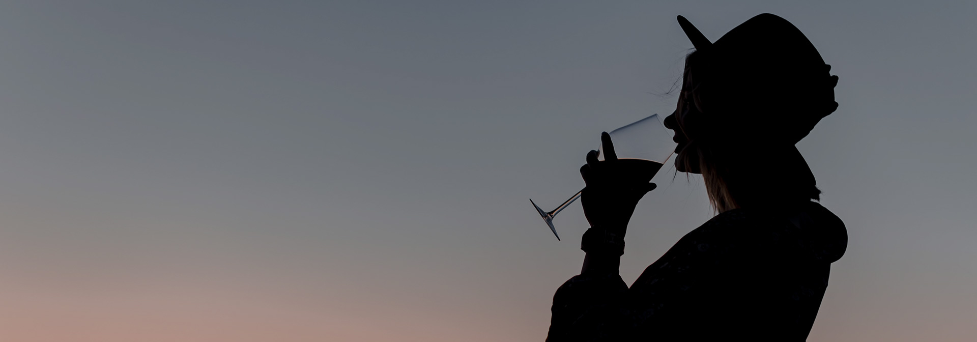 a woman drinking a glass of wine at dusk