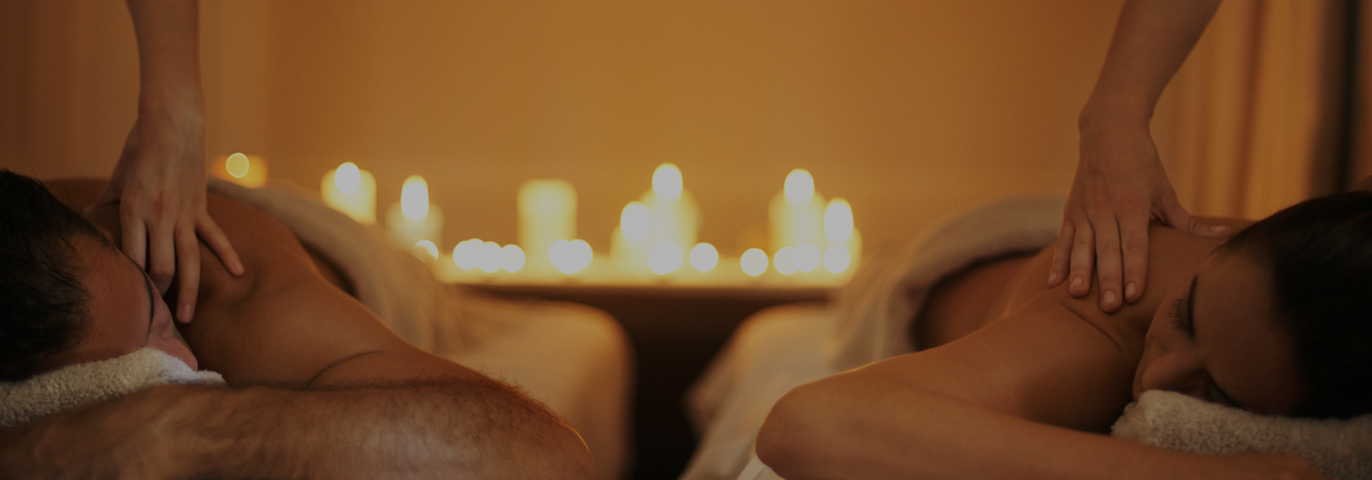 a man and woman laying down and getting massages with many candles lit in the distance