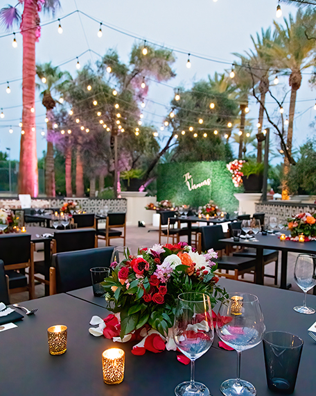 a close up of a table outdoors with red and pink flowers and small tea lights