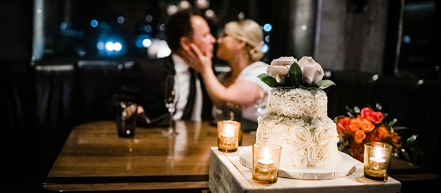 A bride and groom sitting at a booth with dim lighting and a wedding cake