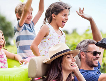 A smiling family driving in a convertible with their hands up in the air.