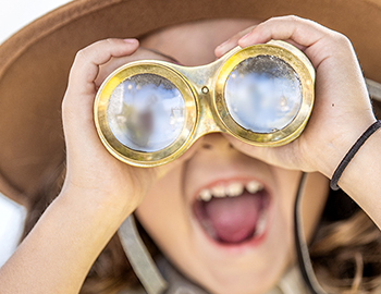 a little girl looking through golden binoculars while smiling