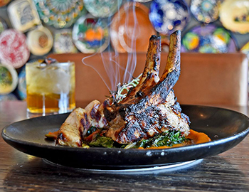 a signature dish with steam coming from it and a small cocktail to the left
