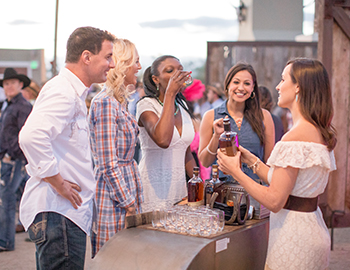 a group of people standing around a bar as one woman takes a shot
