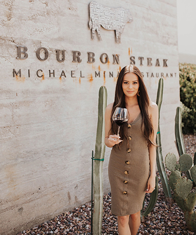 a woman wearing a dress and holding a glass of red wine in front of bourbon steak