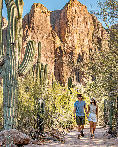 a man and woman holding hands while walking on a path through the desert