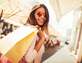 woman in sunglasses smiling while carrying a shopping bag