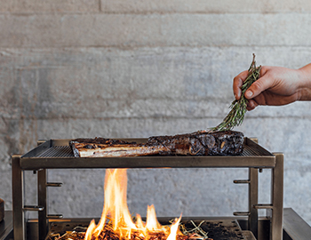 chef cooking a short rib over an open fire pit
