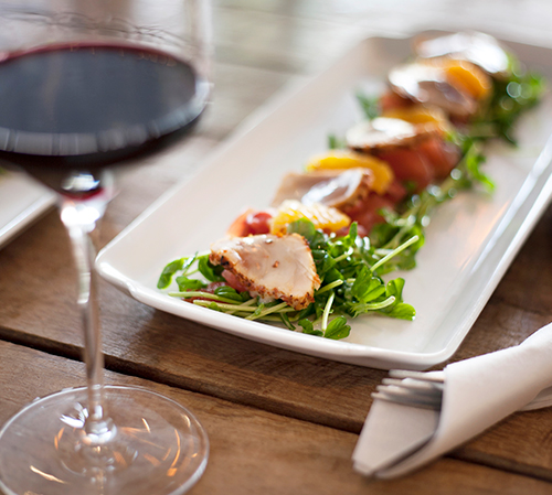 Tender meat and vegetables sliced onto plate next to glass of wine