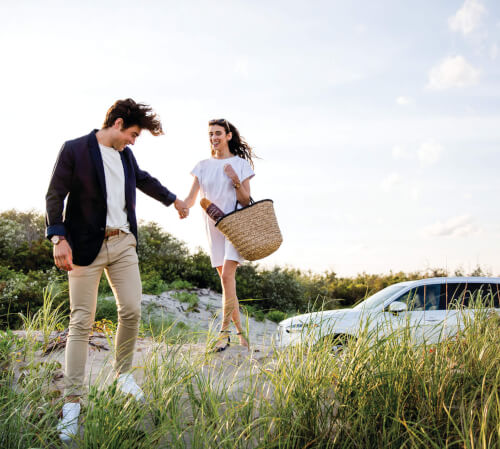 a couple at the beach with a white volvo in the background