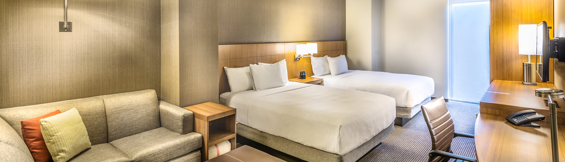 hotel room with two crisp beds and a beige sectional