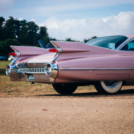 Rear end of pink muscle car on gravel road in green field