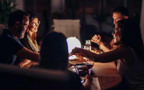 five people gathered around a dinner table in dim light