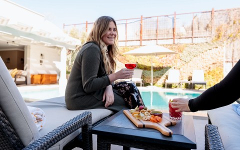 a woman sitting next to a pool holding a glass of red wine smiling