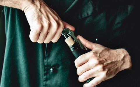 a man opening a bottle of wine with a wine opener 