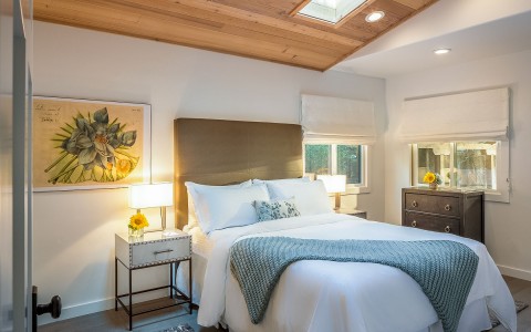 a bedroom with a wooden ceiling that features a bed with white bedsheets and a grey/blue throw
