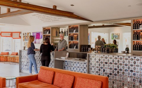 two women speaking to a man in a wine tasting room with orange couches