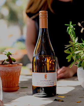 view of a bottle of epiphany wine on a table with a woman in the background