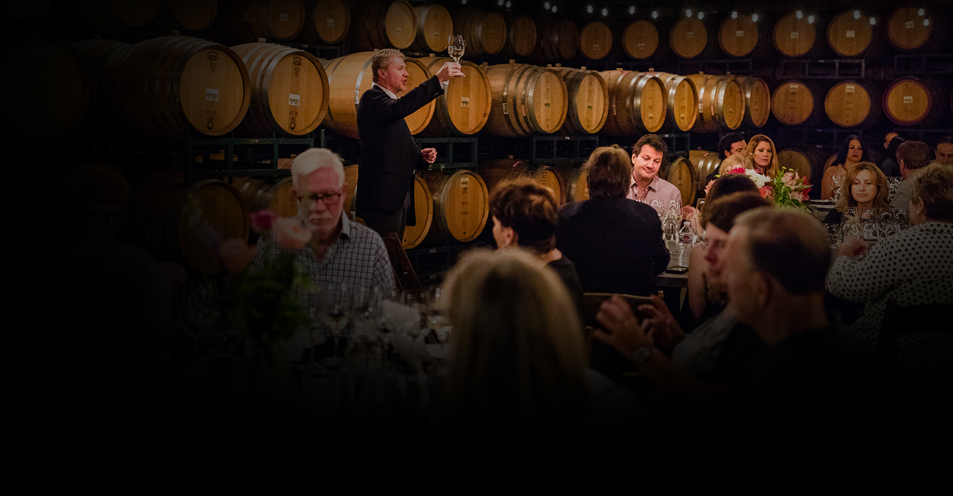 a man toasting to a room full of people sitting down at tables