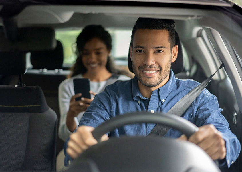 man driving a young woman on her phone in the back