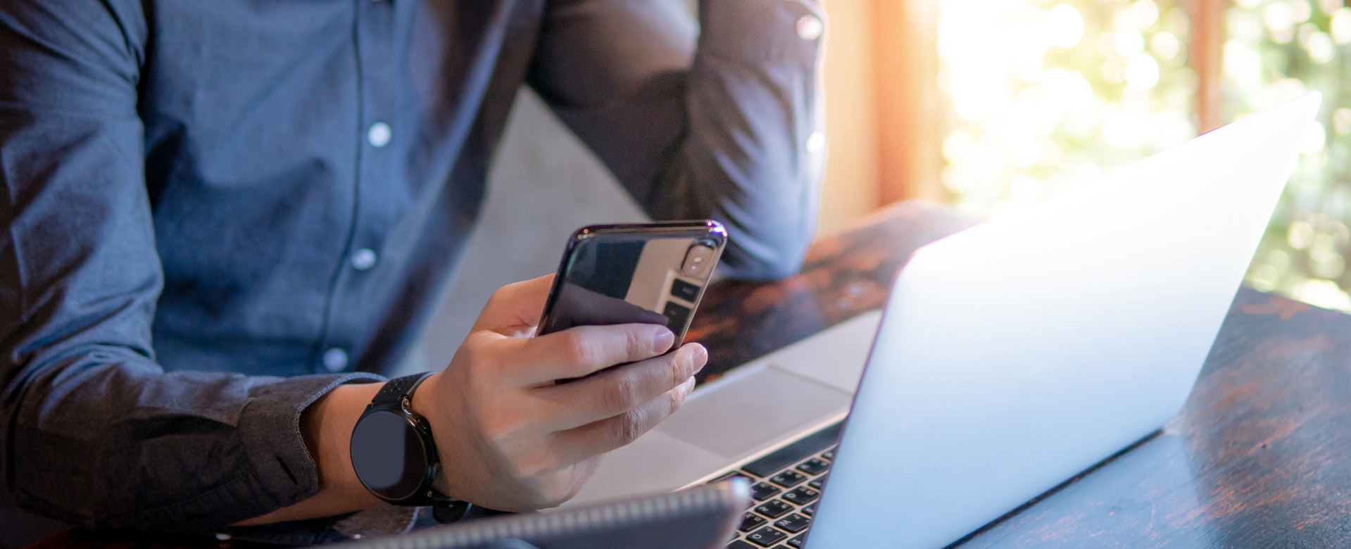 man holding his smartphone while sitting with his laptop