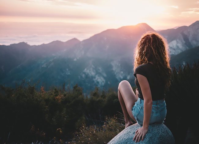 woman sitting on rock on top of mountain looking at sunset