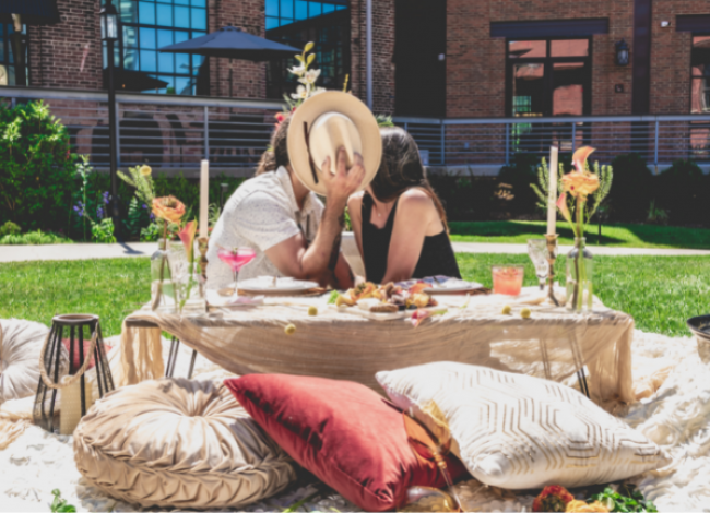 couple on picnic kissing behind hat