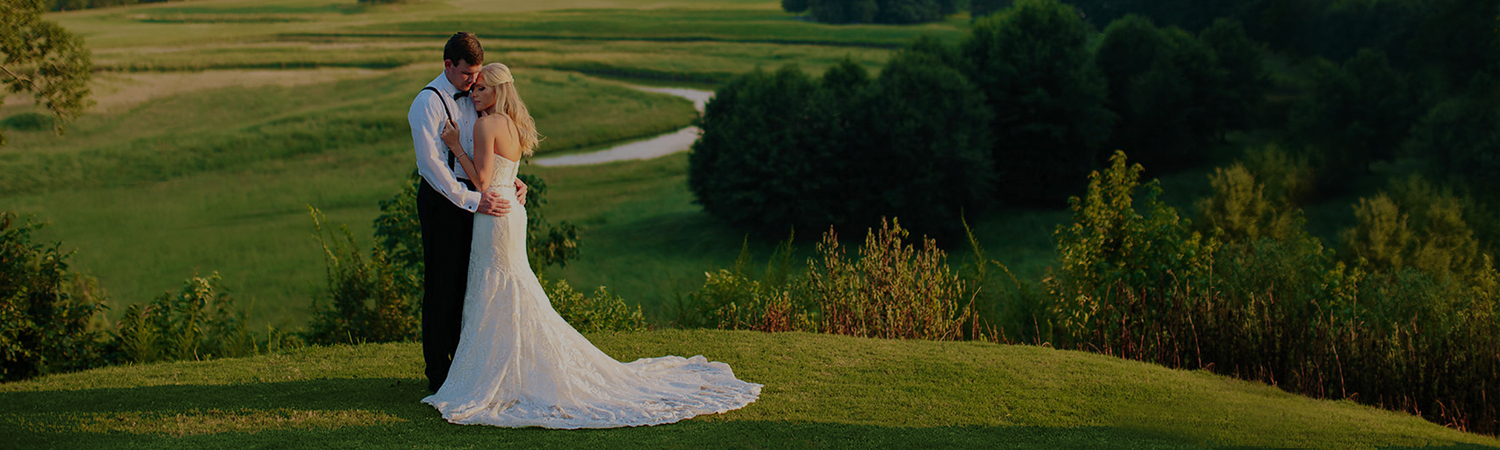 Wedding hugging & standing on vast green field with trees in the distance