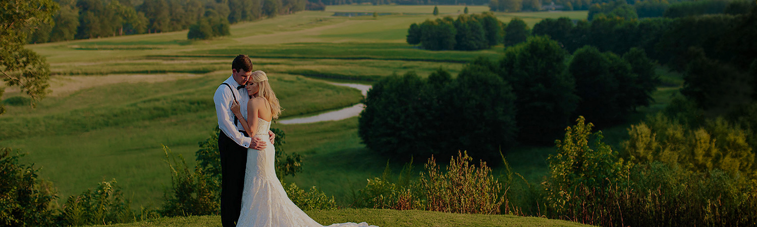 Wedding hugging & standing on vast green field with trees in the distance