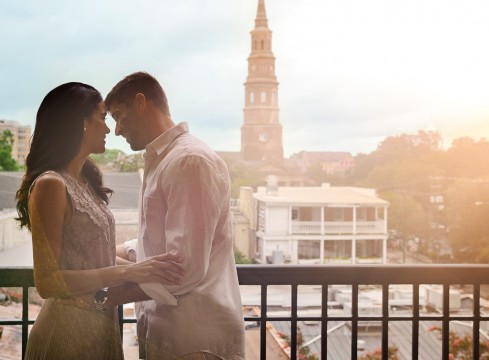 Couple looking into each others eyes and smiling out on the balcony with the town of St. Augustine in the background